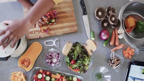 Overhead-view-of-african-american-woman-cooking-in-kitchen,-composting-vegetable-waste,-slow-motion