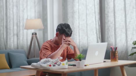 아시아 소년 신발 디자이너가 집에서 노트북으로 일하면서 두통을 고 있습니다.
