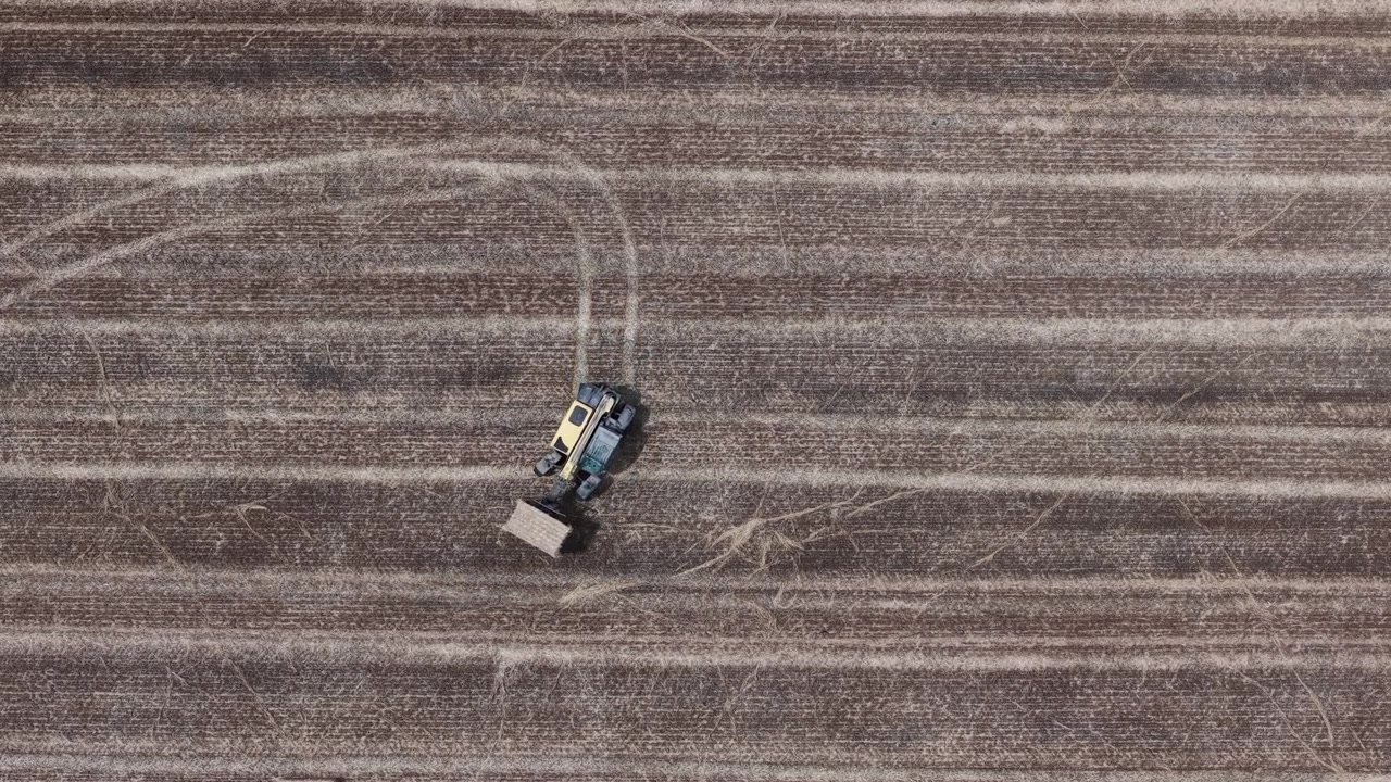 Una macchina agricola imballa efficientemente stoppie essiccate in un vasto campo raccolto, ripresa da una prospettiva aerea, mostrando le moderne operazioni agricole.