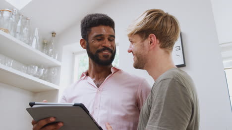 male gay couple using digital tablet at home in kitchen together