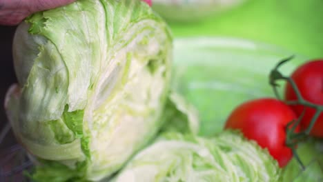 head of fresh green lettuce veggies being sliced chopped up with fresh red tomatoes in background of close up shot during barbecue backyard party, close up shot slowed halfway from 60fps