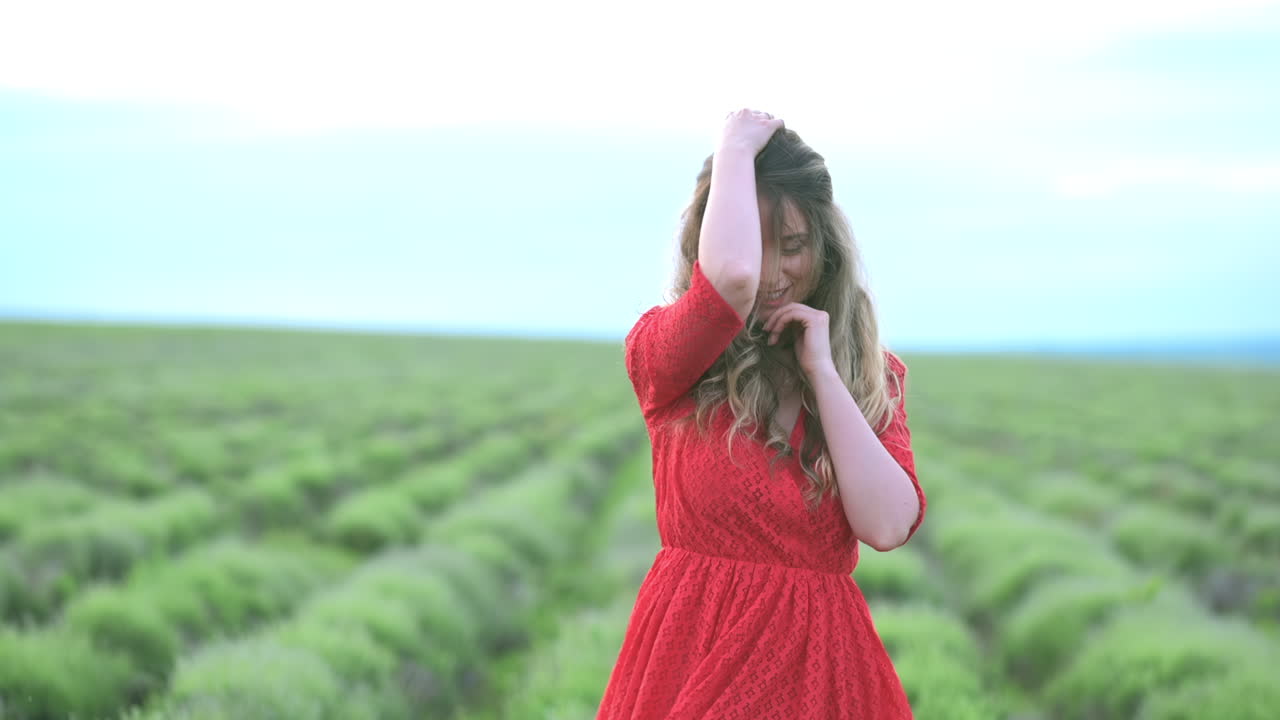 A woman in a red dress walks through a lush green field with the wind in her hair