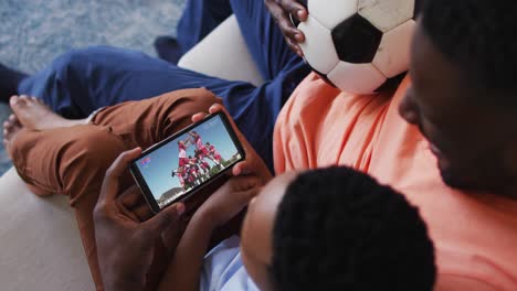 Composite-of-father-and-son-at-home-watching-sports-event-on-smartphone