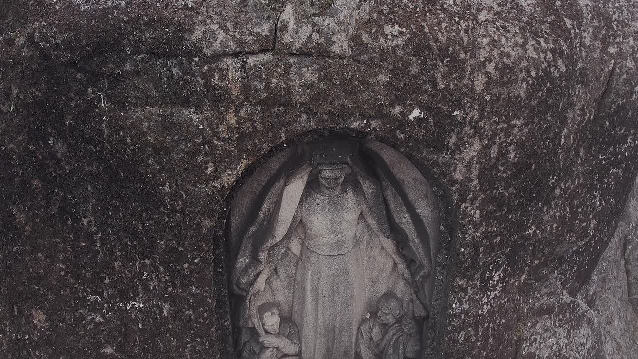 Statua di Nossa Senhora da Boa Estrela scolpita in una nicchia di granito nella Serra da Estrela, Portogallo, che mostra una scultura religiosa incastonata nella parete rocciosa con texture erosa e simbolismo sacro, in discesa.
