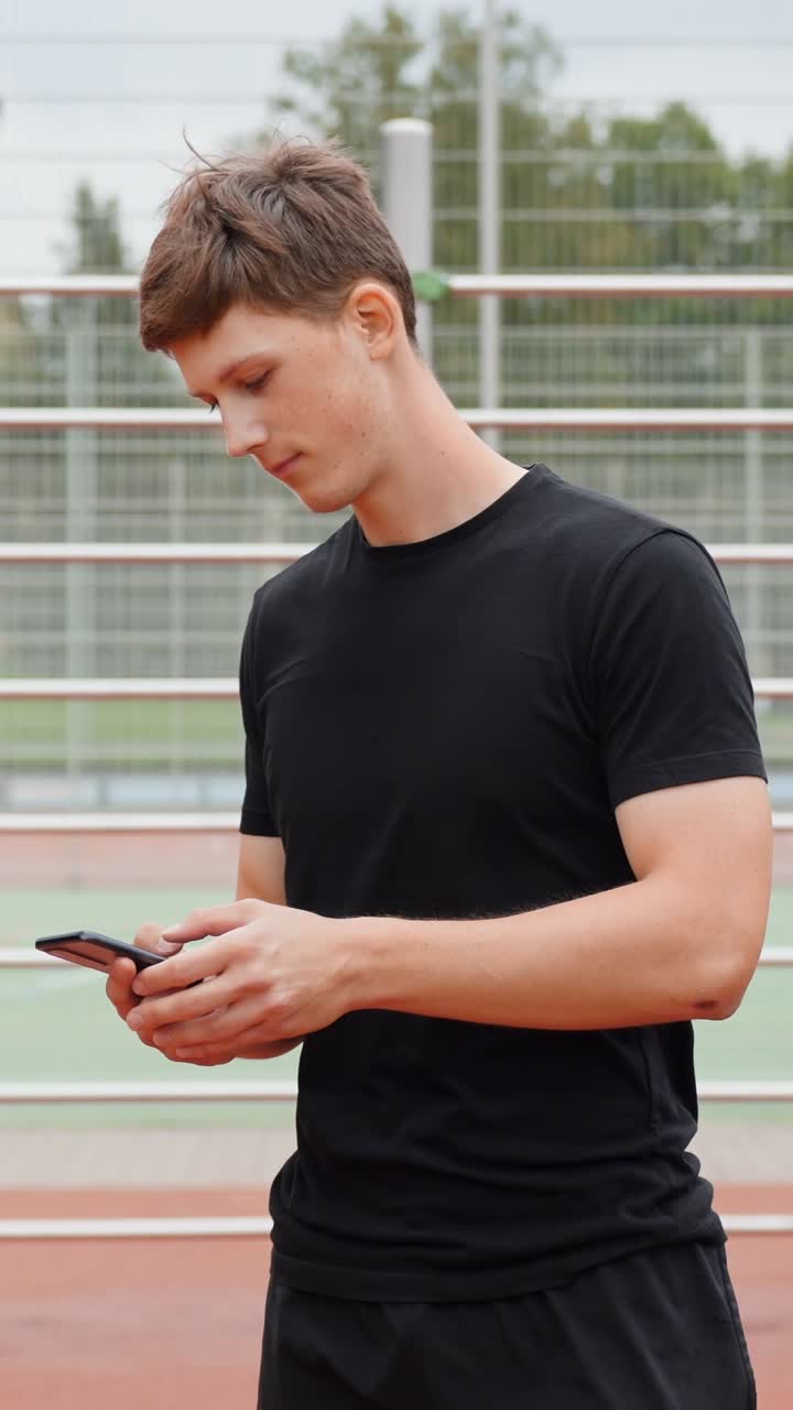 Young man in sports outfit using smartphone outdoors on track
