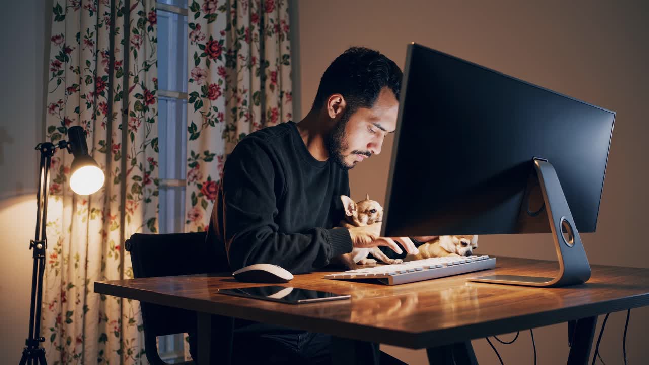 Nighttime workspace harmony, man working on computer, small dog resting comfortably in arms, creating peaceful home office atmosphere