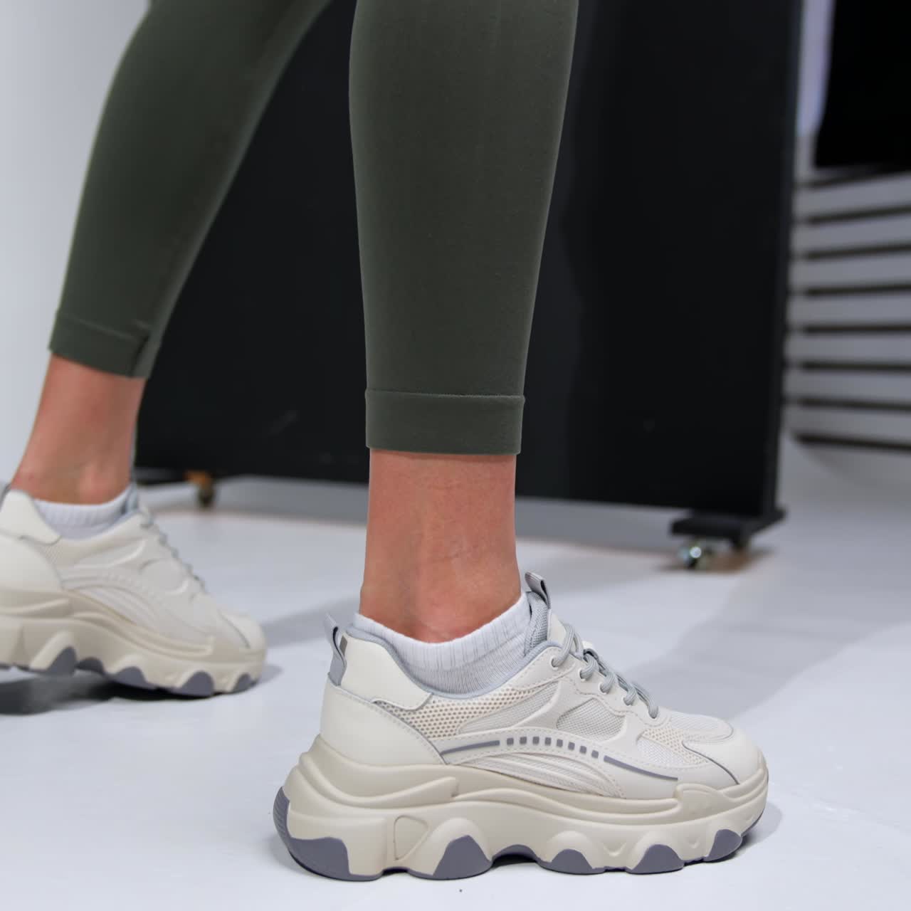Lady in dark green leggings and white trendy sports shoes. Close up. Studio footwear demonstration
