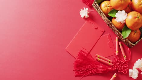 Video-of-envelopes,-oranges-and-flowers-on-red-background