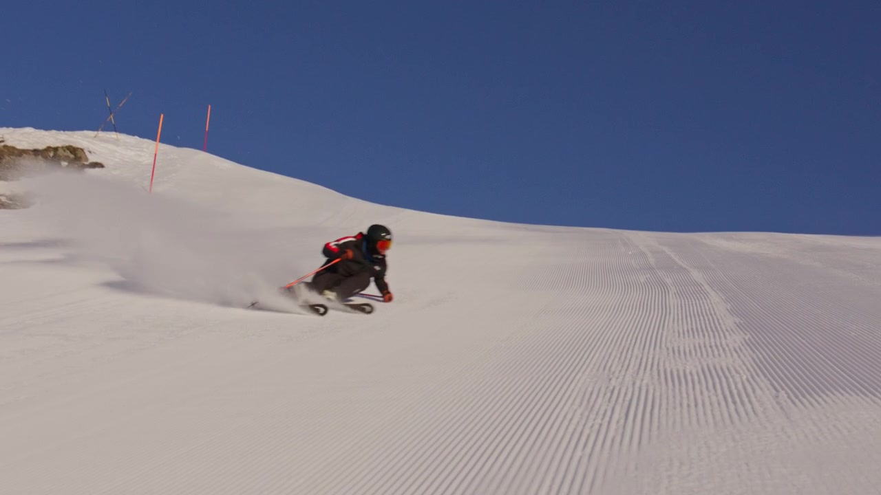 Sciatore che intaglia piste battute ad alta velocità a Nendaz, parte del comprensorio sciistico 4 Vallées nelle Alpi svizzere. Sci alpino d'élite con potenti spruzzi di neve e tecnica di precisione.
