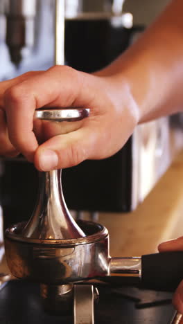 camarero usando un manipulador para presionar el café molido en un portafilter