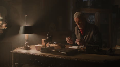older passionate man evaluates an old silver skull watch in his office at night