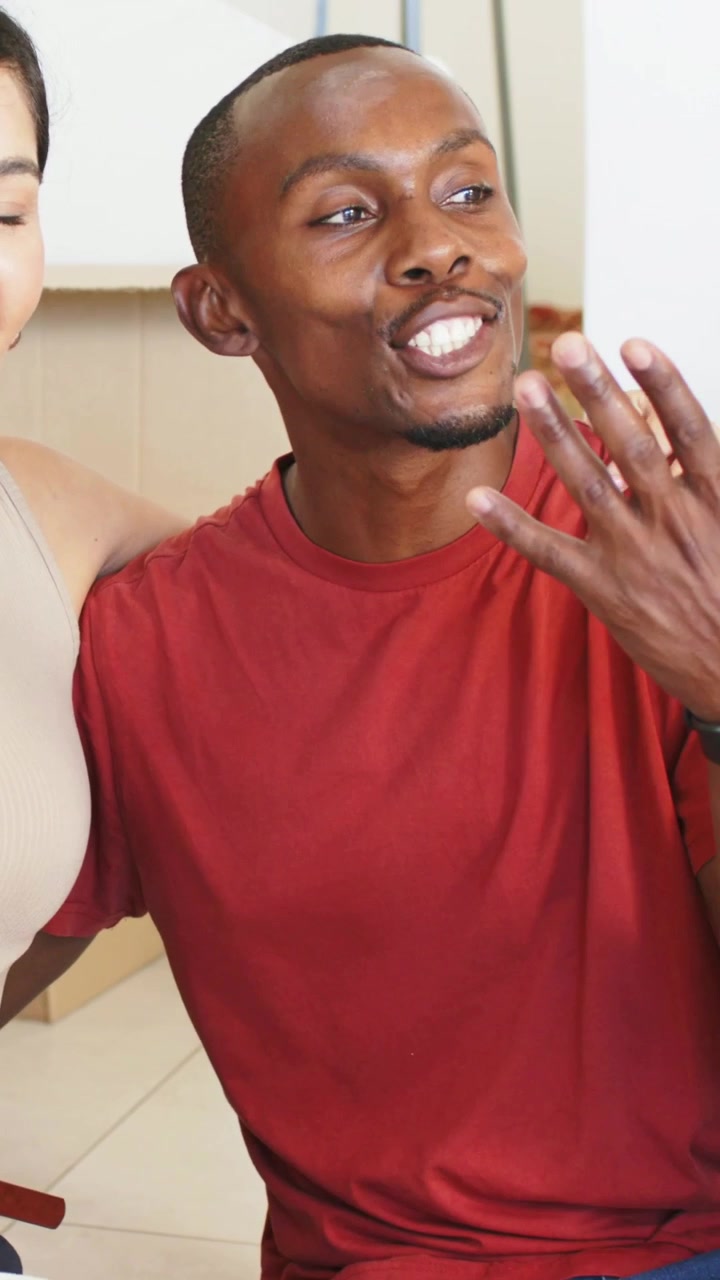 Vertical video: Smiling woman in beige top holding white mug, reacting warmly as man entering right