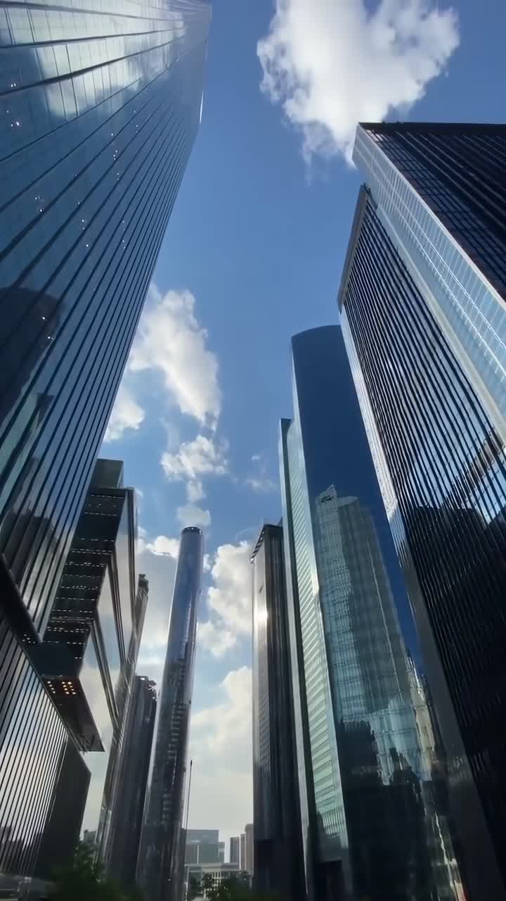 Vídeo em ângulo ascendente de arranha-céus modernos contra um céu azul, capturando a arquitetura urbana
