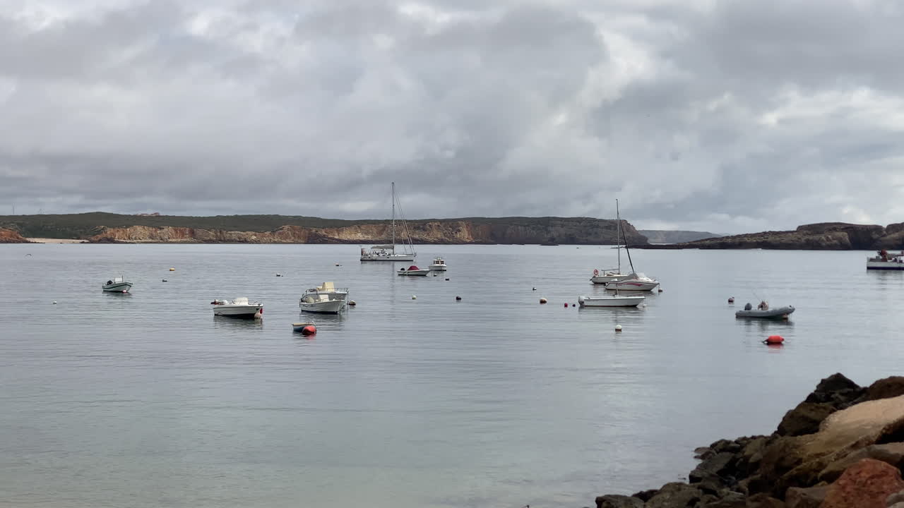 panning View of Sagres harbor framed by rocks and distant cliffs under a moody Atlantic sky