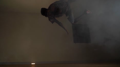 Slow-motion-shot-of-African-youth-in-a-beanie-doing-a-very-large-kick-jump-and-spin-in-the-air-in-colorful-disco-lights-and-smoke