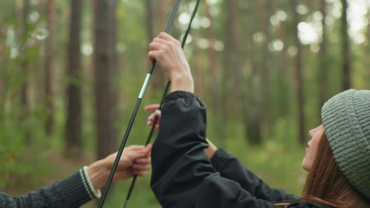 Young couple collaborates outdoors in lush forest as they connect tent poles during camping setup, focused and coordinated in preparation for adventure surrounded by nature and trees