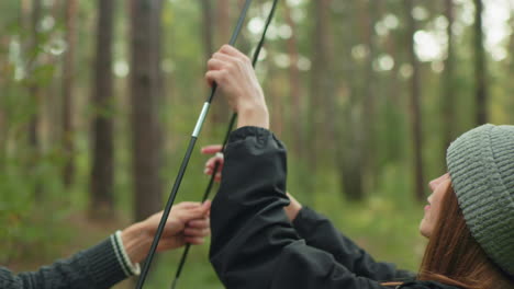 young couple collaborates outdoors in lush forest as they connect tent poles during camping setup, focused and coordinated in preparation for adventure surrounded by nature and trees