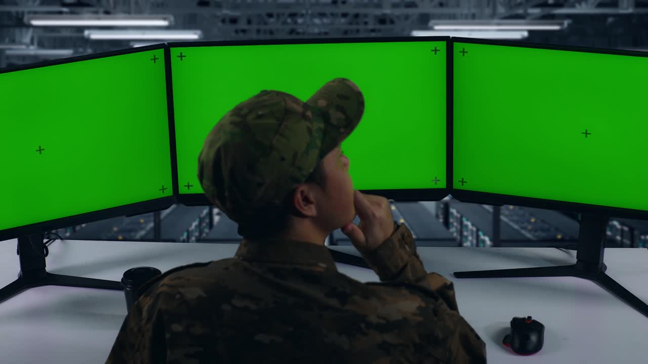 vista de atrás de los militares asiáticos pensando en algo mientras trabajaba con simulacro de varios monitores de computadora en el centro de datos