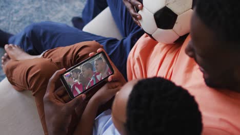 Composite-of-father-and-son-at-home-watching-sports-event-on-smartphone