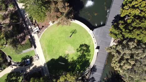 aerial ascending view over circular grass area of landscaped park with fountains