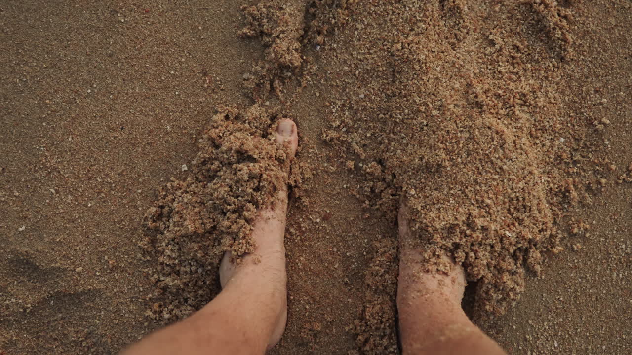 Piedi sepolti nella sabbia, viaggiatore che si radica su una spiaggia calda, primo piano delle dita dei piedi e dei granelli di sabbia testurizzati, bagliore del tramonto, movimento lento e meditativo, rituale di benessere e pacifica solitudine marina.