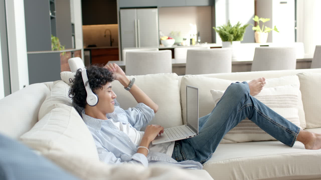 Relaxing on sofa, teenage boy using laptop and wearing headphones at home