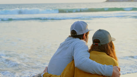 Vista-Trasera-De-Una-Joven-Pareja-Caucásica-Sentada-En-Una-Roca-Y-Mirando-El-Mar-En-La-Playa-4k