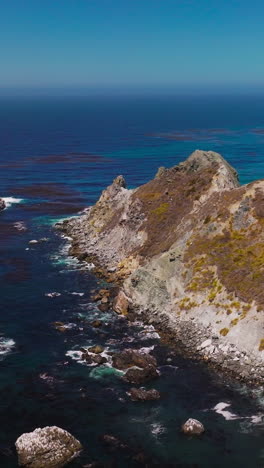Rocks overgrown with moss surrounded by blue deep waters. Stunning seascape with hazy line of horizon on sunny day. Vertical video