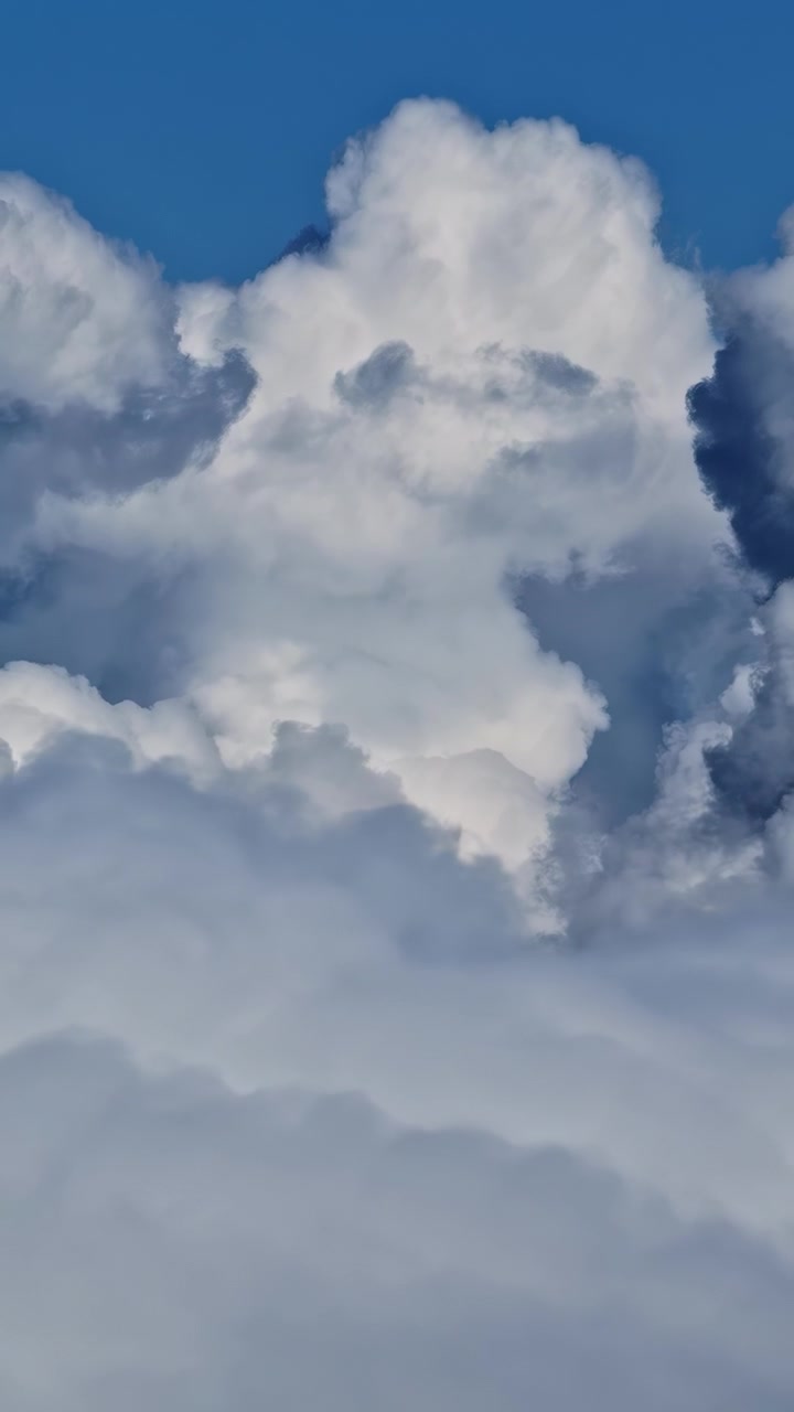 Large white cumulus clouds forming against bright blue daytime sky, vertical peaceful backdrop
