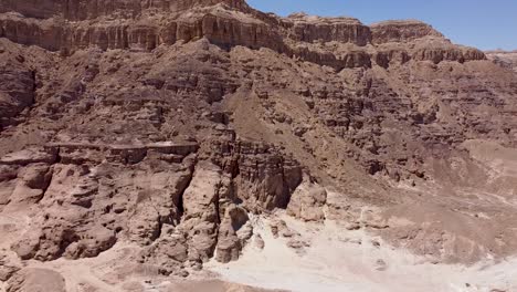 Aerial-slow-and-calming-backward-drone-shot-of-a-boulder-ridge-in-the-middle-of-a-desert,-surrounded-by-sand-and-dirt