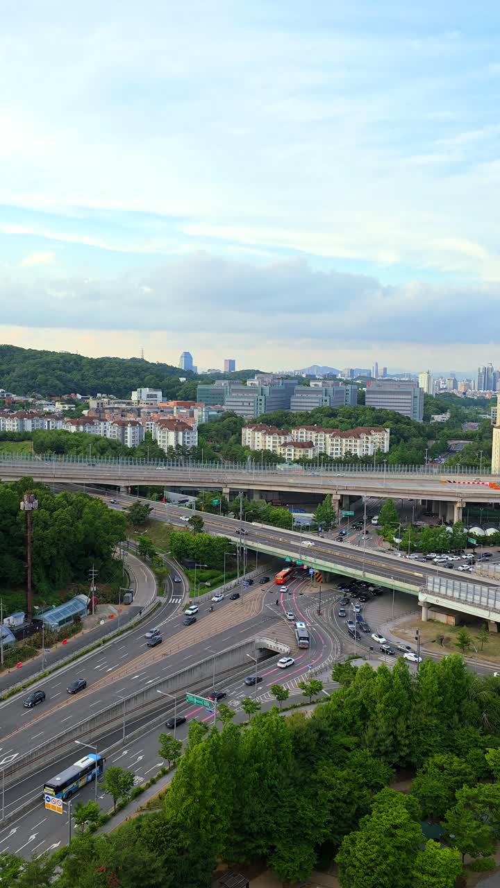 A high-angle vertical shot of the modern urban landscape of Seocho-gu, Seoul, showing a complex highway interchange with traffic, surrounded by green trees and buildings