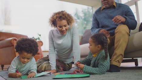 Großeltern-Sitzen-Zu-Hause-Mit-Enkelkindern-Auf-Dem-Boden-Und-Zeichnen-Gemeinsam-Ein-Bild