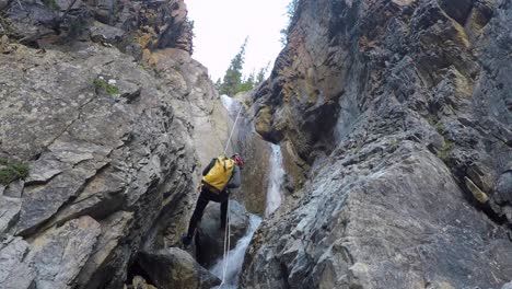 male canyoneer with pack rappels rope down river waterfall in canyon