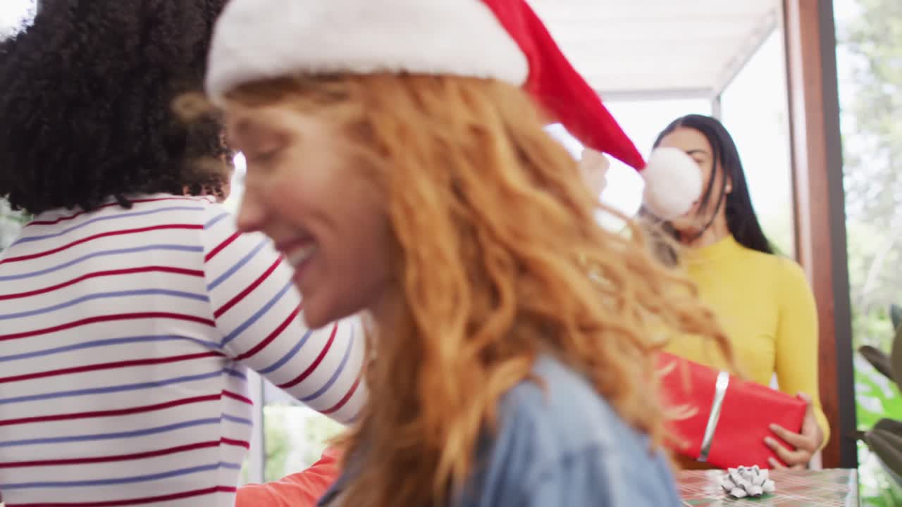 Blije biculturele vrouw begroet diverse vrienden met kerstmutsen en kerstcadeaus bij de voordeur