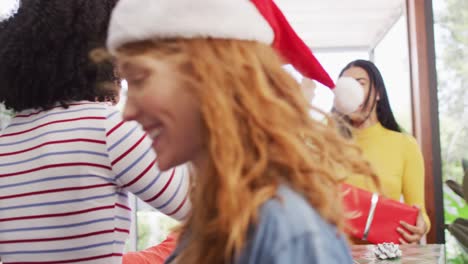 una mujer biracial feliz saludando a amigos diversos con sombreros de santa con regalos de navidad en la puerta principal.