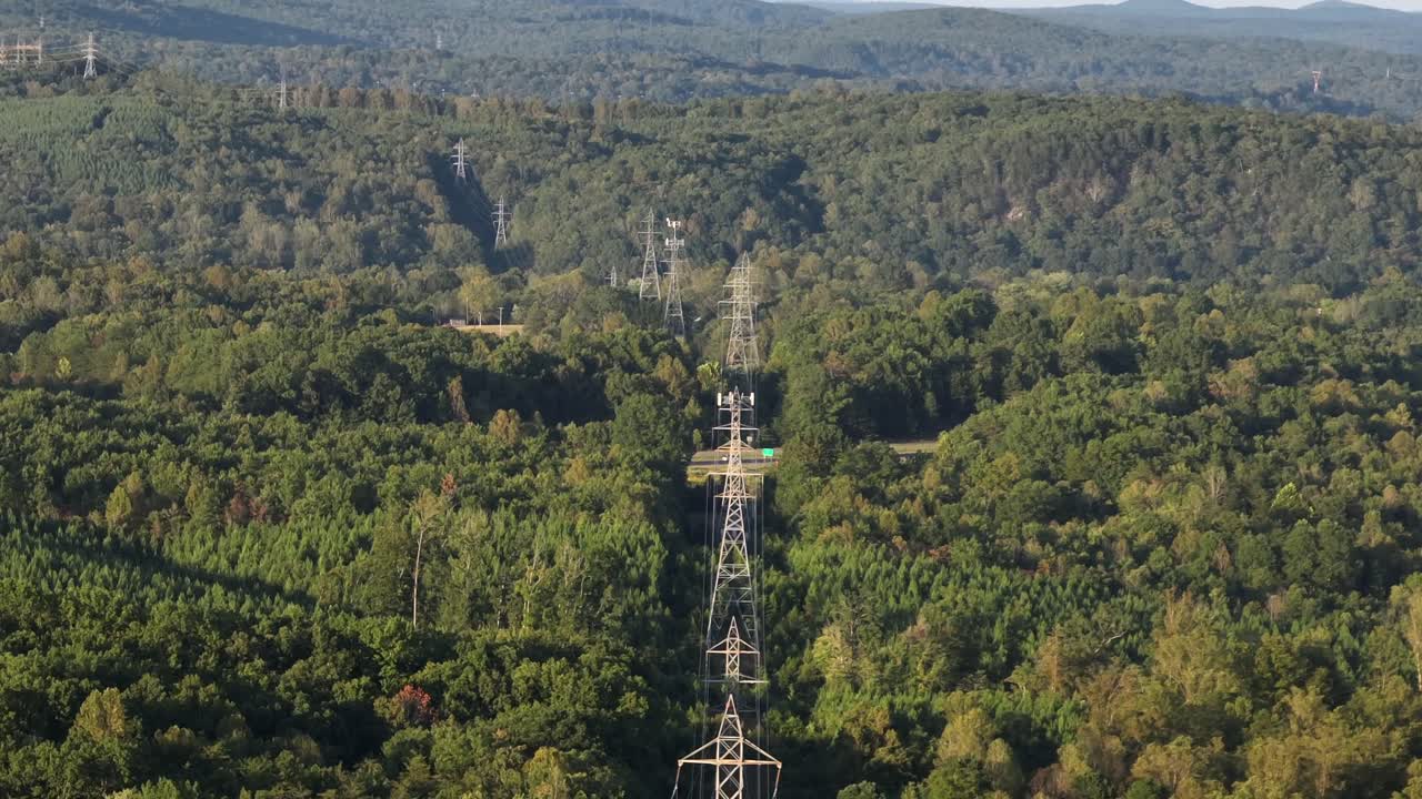 Electric power lines between green lush trees of blue ridge mountains in Virginia, USA. Traffic on highway in background. Sunny day in summer. Wide shot