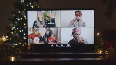 toma deslizante acercándose a la pantalla del portátil con pantalla dividida en 4 vías de amigos levantando gafas en videollamada