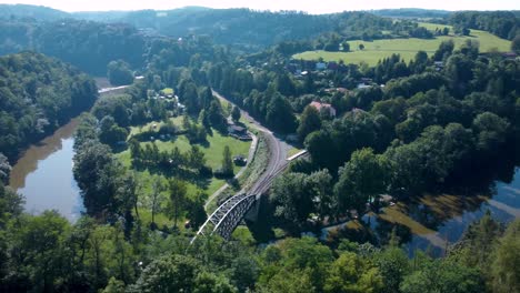 Antena-De-Un-Puente-Ferroviario-Sobre-Un-Río-Con-Reflejos-Solares-Y-Bosques-Alrededor