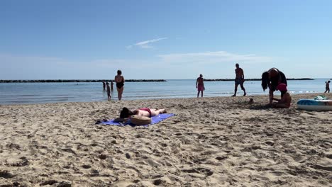 a serene beach scene featuring people relaxing on the sandy shore and swimming in calm waters. various individuals are sunbathing, playing, and enjoying a sunny day by the seaside