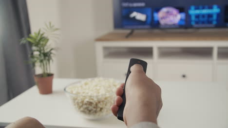 someone's hand with a remote control navigates through the tv menu for a programme or film to watch