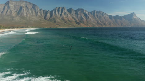 surfistas en la playa de la bahía de kogel con vistas a las montañas de kogelberg en ciudad del cabo, sudáfrica