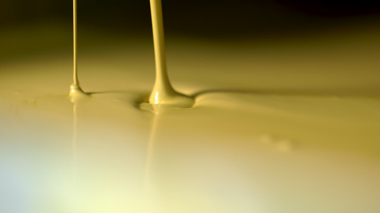 Camera pan up to an extreme closeup of pale yellow paint endlessly pouring out of a valve