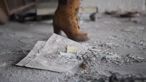 a close up shot a woman with a pair of suede brown boots, kicking a pile of dust and trash aggressively