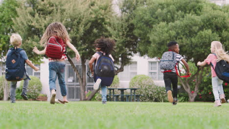 rear view of  elementary school pupils running across field at break time