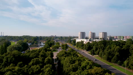 Aerial-forward-flight-over-tree-avenue-beside-River-and-highway-in-Warsaw-Suburb-area---Three-high-rise-apartment-complex-in-Background