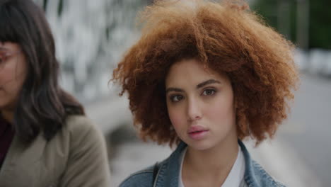 retrato de una atractiva mujer joven de raza mixta mirando a la cámara pensativa calma linda estudiante femenina roja afro peinado rizado en la calle de la ciudad urbana
