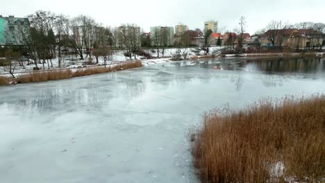 A-freezing-lake-in-an-urban-park,-with-a-busy-city-street-in-the-background