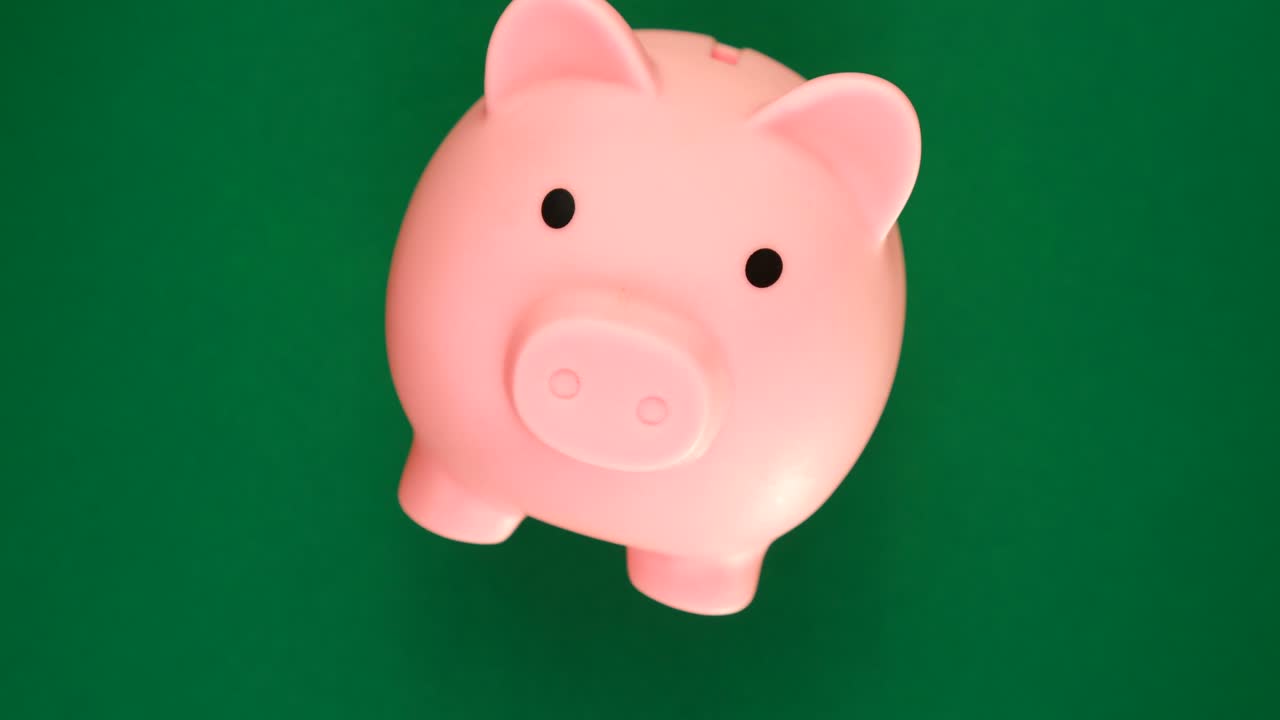 la rotación de la alcancía rosa en el fondo de la pantalla verde de la llave de croma. concepto de ahorro de dinero.