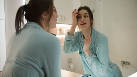 A-young-woman-looks-in-the-mirror,-preens-herself,-admires-herself-and-smiles