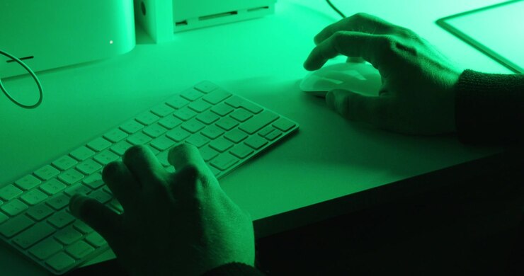 Close-up van handen die een computertoetsenbord en muis bedienen onder dramatische groene verlichting. Concepten als computergebruik, productiviteit, programmeren, technologie en digitale werkruimte